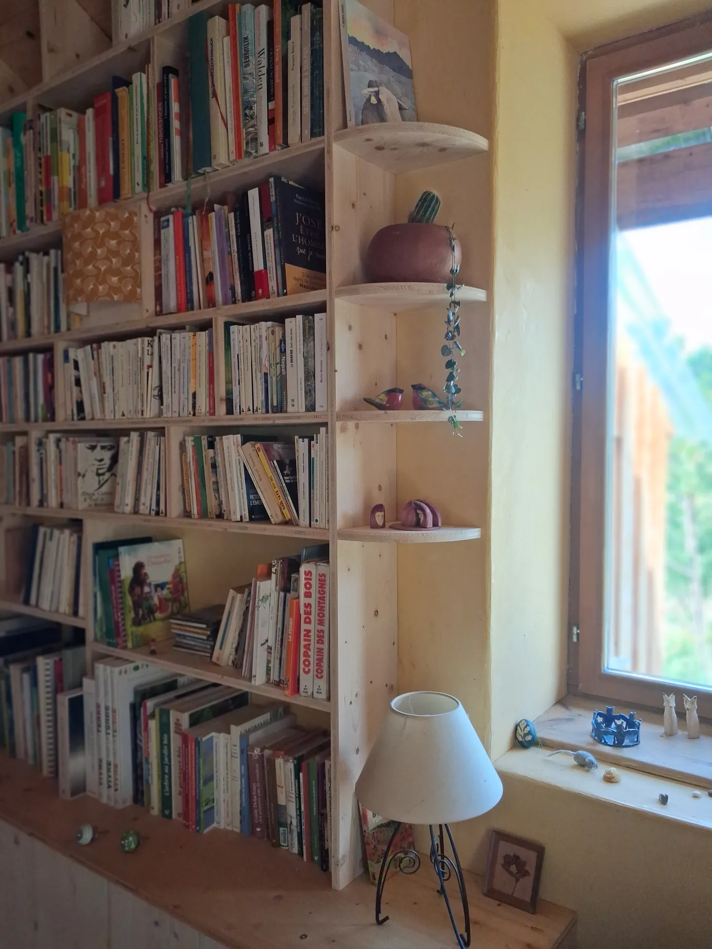 The upper part of the bookcase follows the sloping ceiling, rounded shelves at the end near the window