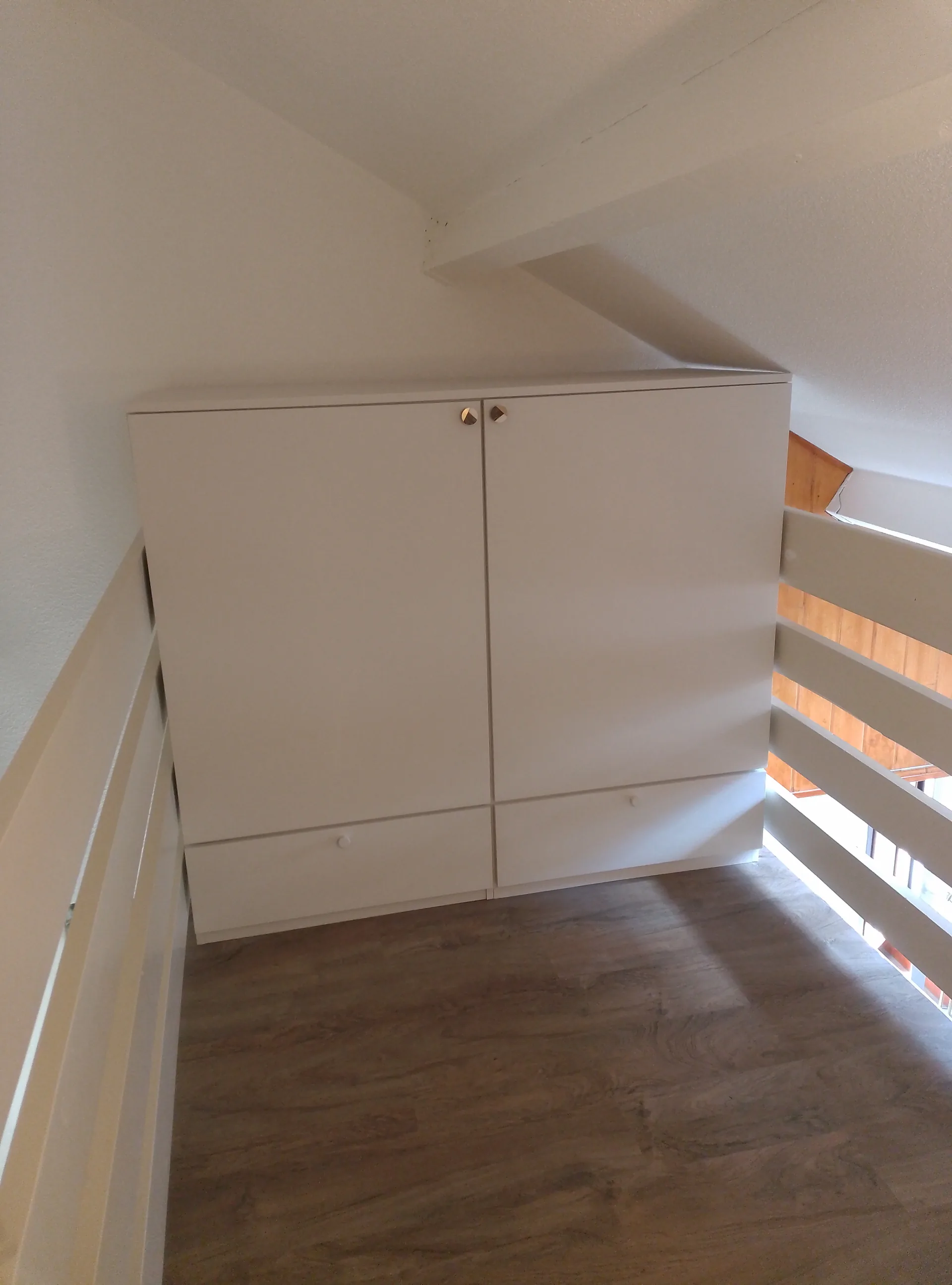 Landing storage unit in white painted MDF, doors closed, between the railings of the floor