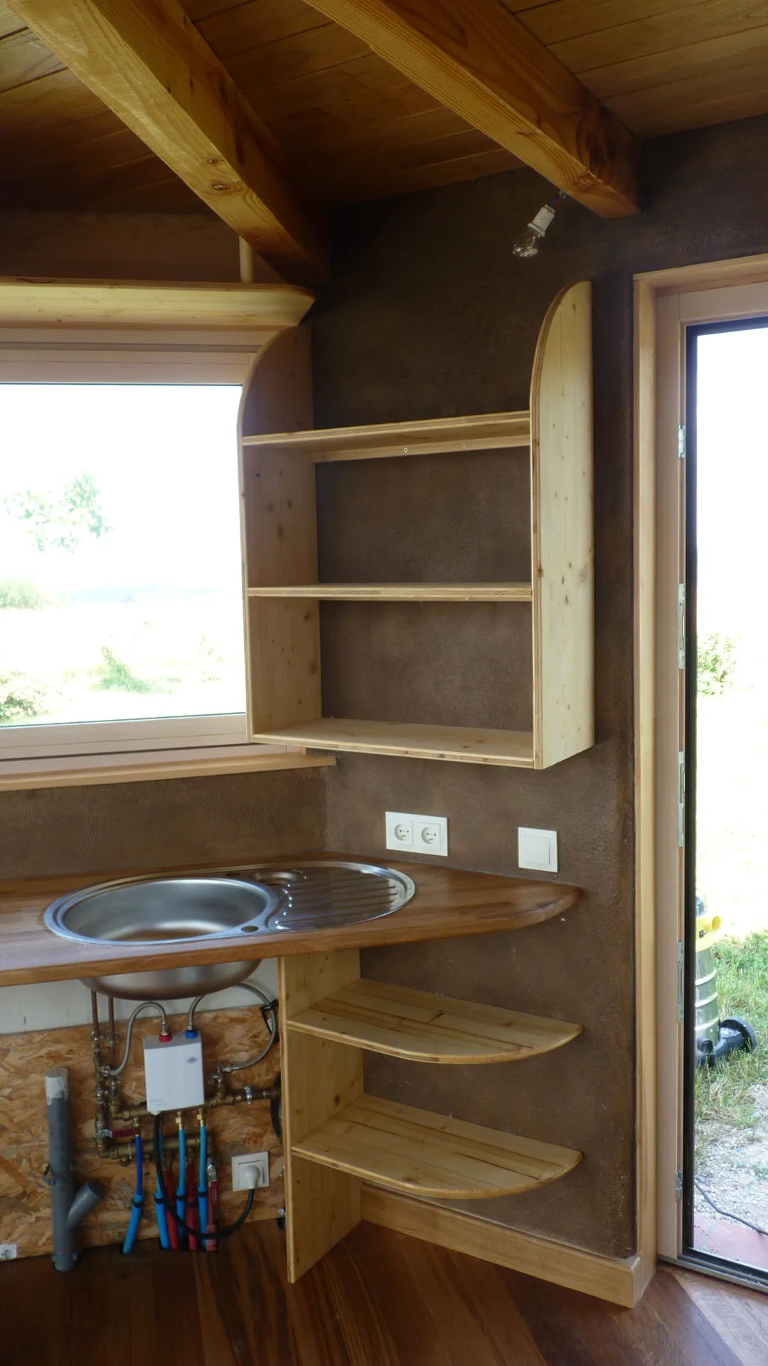 The full arrangement on the sink side: oak worktops, rounded shelves, lime-plastered walls