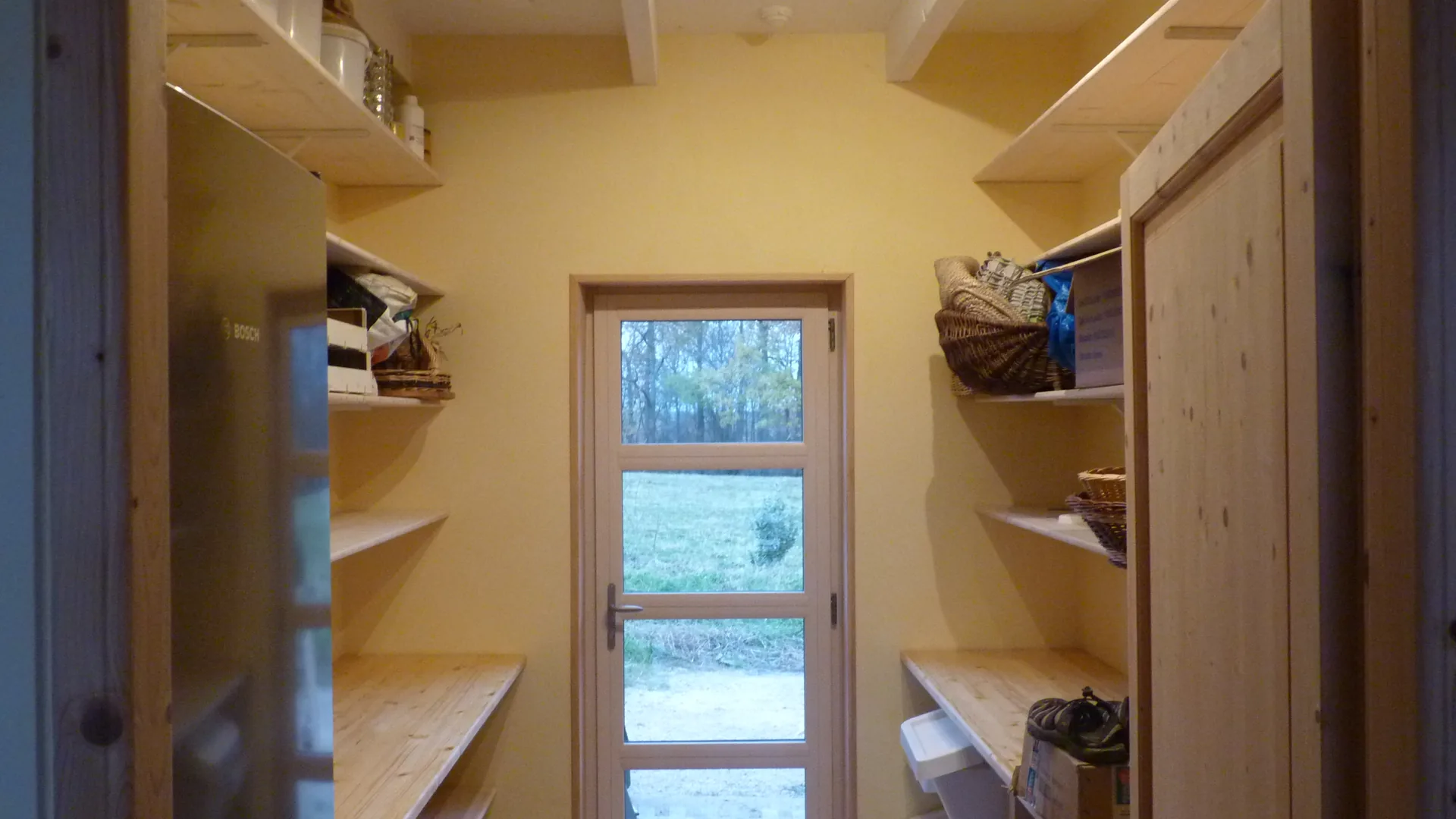 The pantry seen along its length: shelving on both sides up to the ceiling, a glazed door at the far end